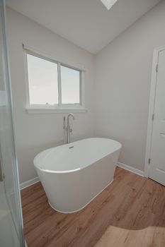 Bright, airy bathroom featuring a sleek freestanding bathtub and wooden flooring.