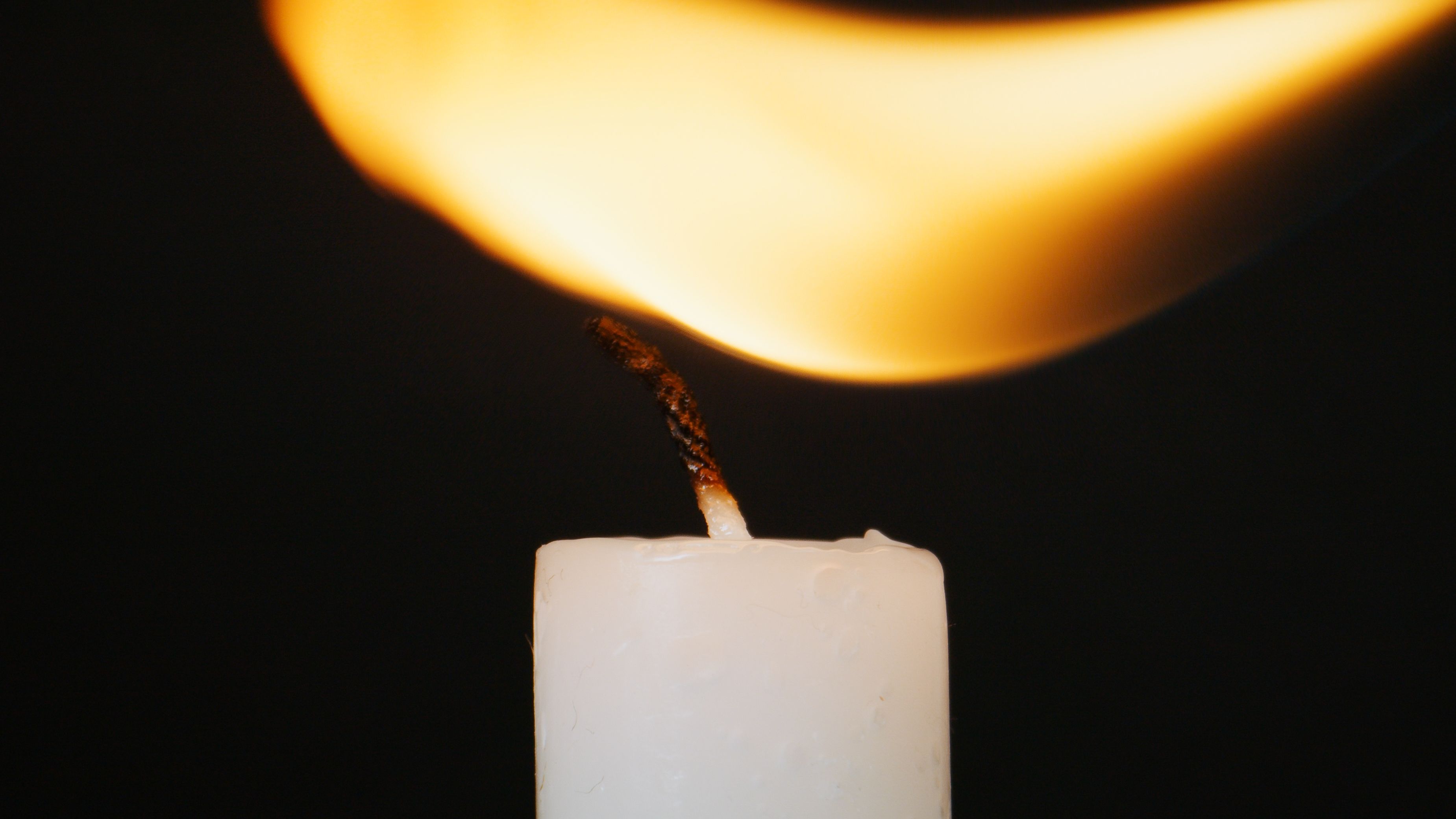 A detailed close-up of a white candle burning against a dark background, highlighting the flame