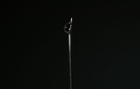 Close-up of a steel needle with a water droplet against a dark background.