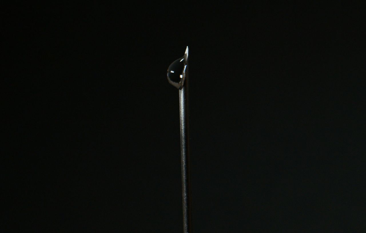 close up of a steel needle with a water droplet against a dark backgro