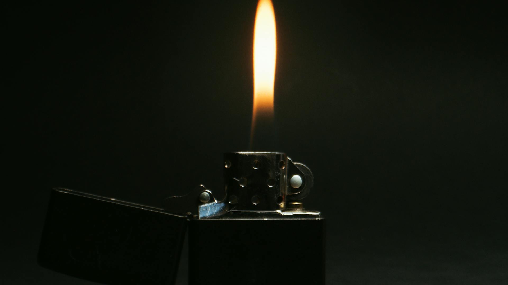 A close-up view of a lit flip top lighter against a dark background.