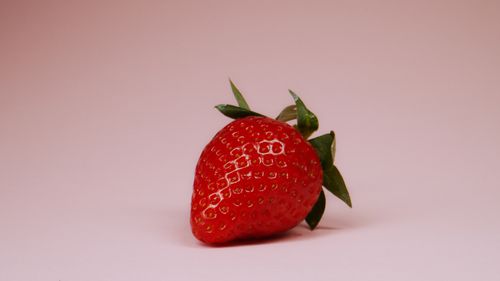 Free A vibrant red strawberry with green leaves on a pink surface, highlighting its freshness. Stock Photo