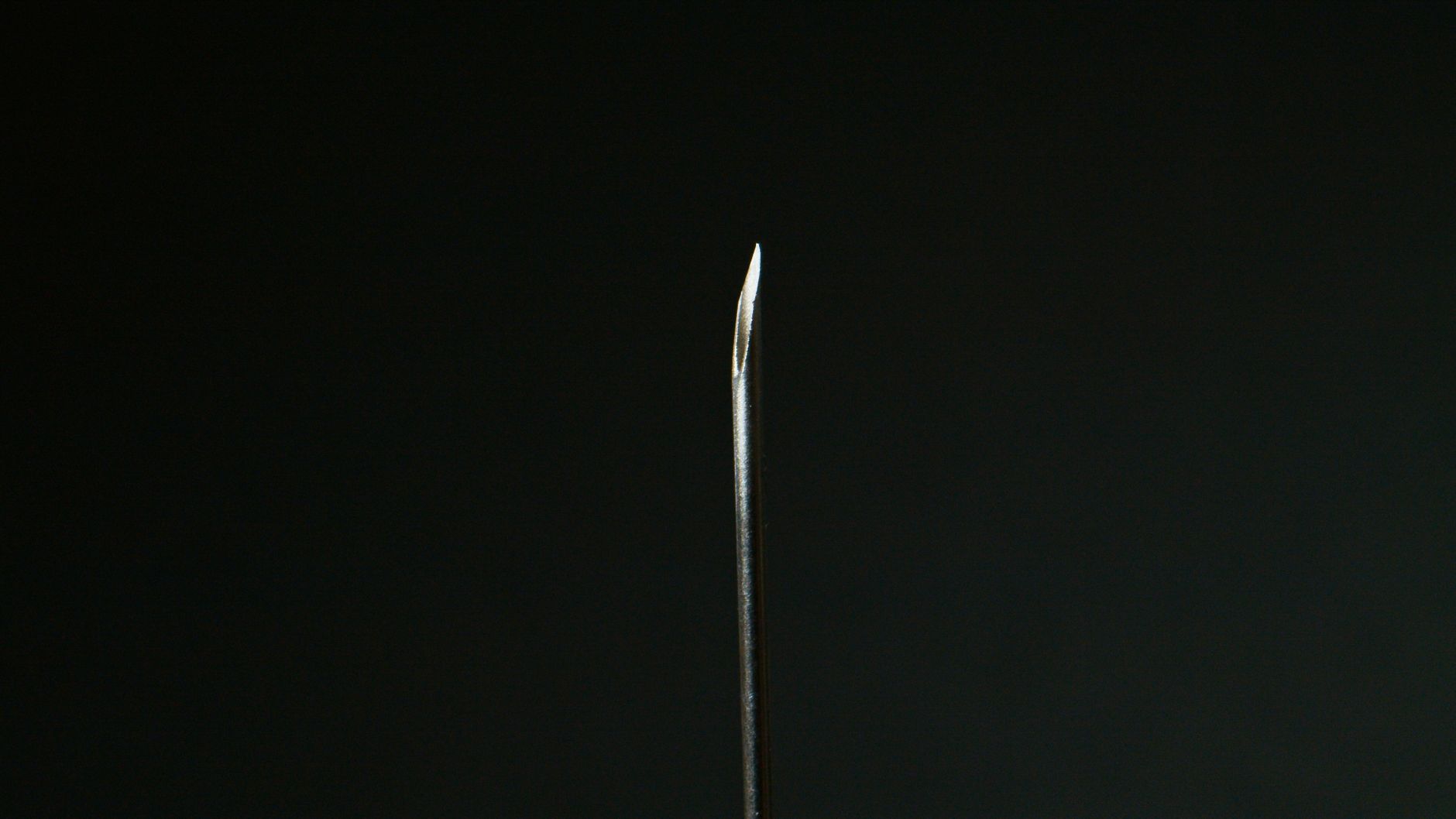 Detailed macro shot of a sharp metal needle against a dark background.