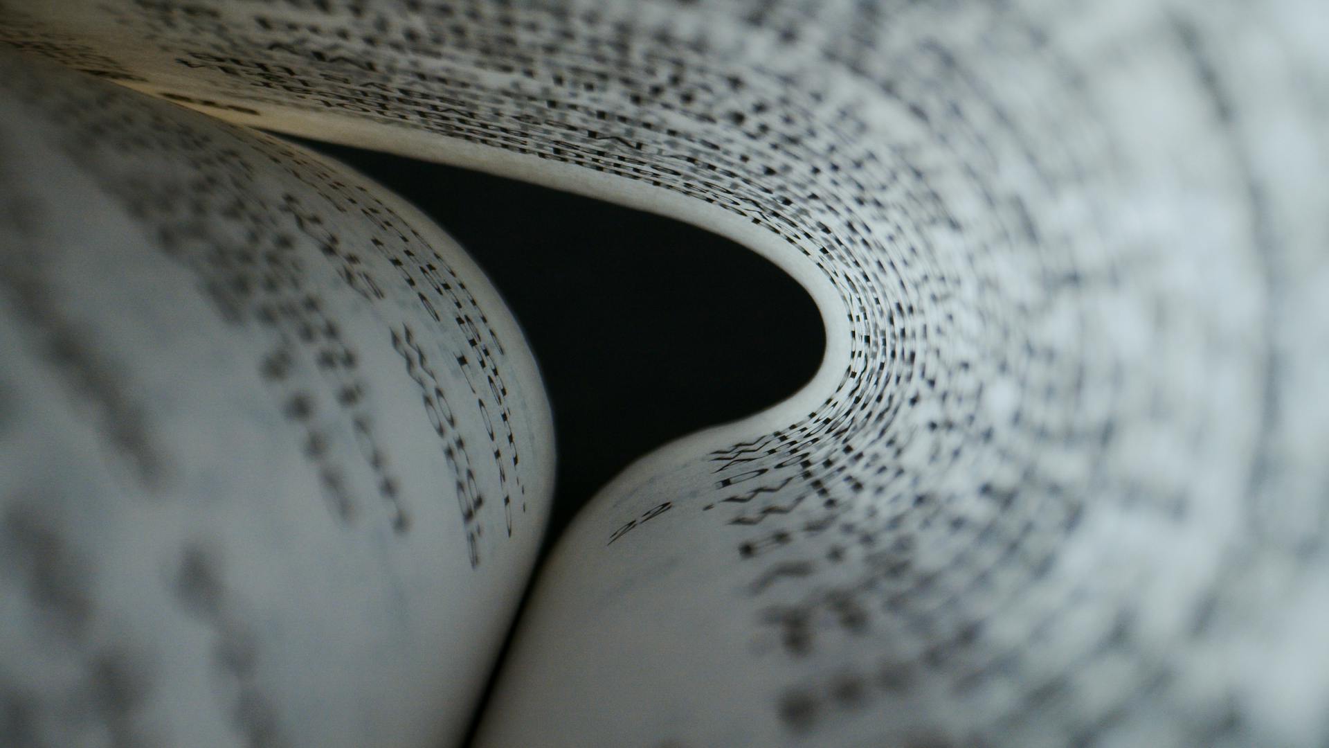 Artistic close-up of book pages forming a curve, showcasing detailed text patterns.