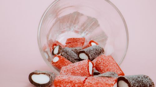 Free Close-up of assorted sour candies spilled from a glass jar against a pink backdrop. Stock Photo