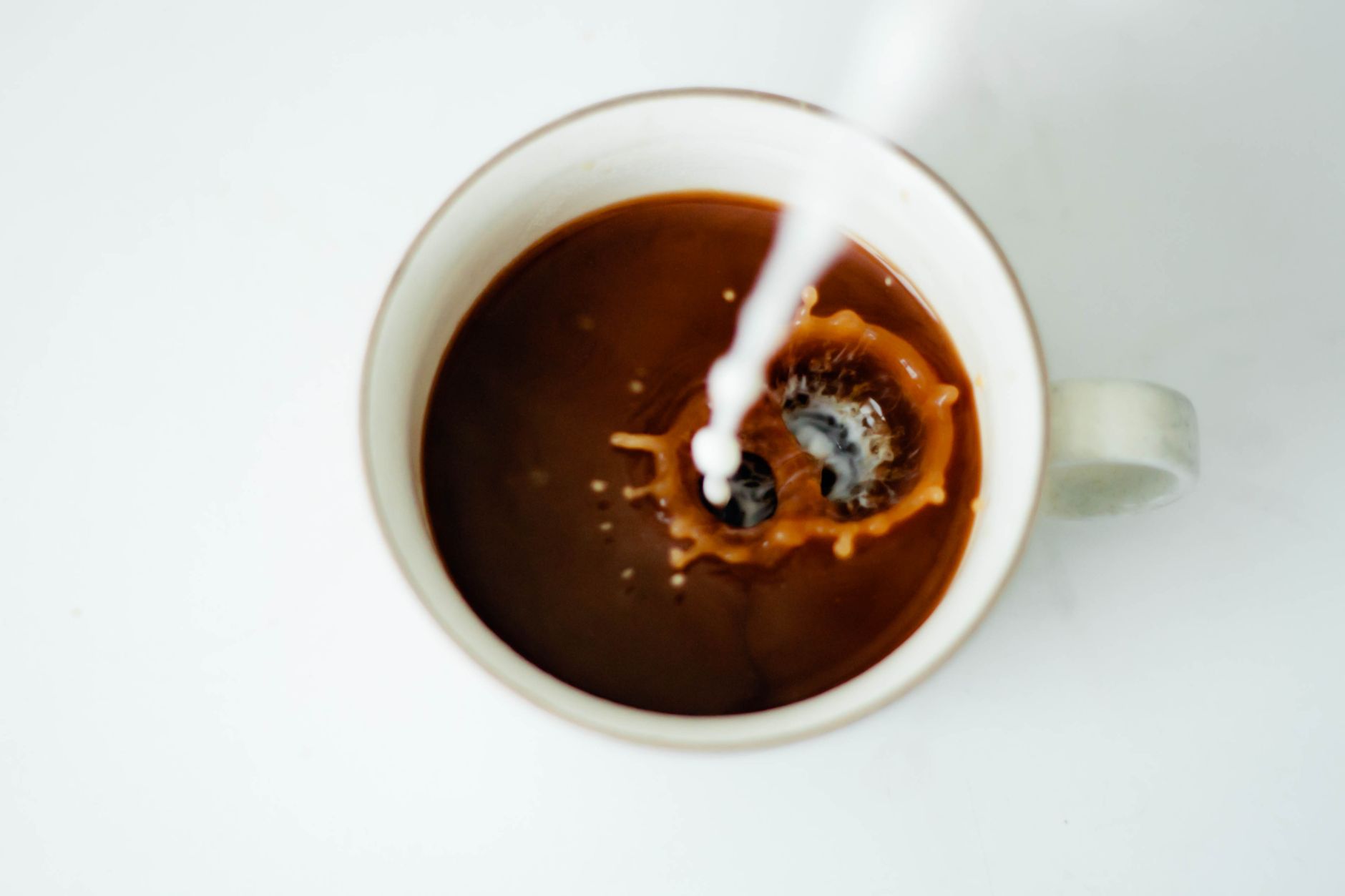 Close-up of milk creating a splash in a coffee cup with white background, shot indoors.