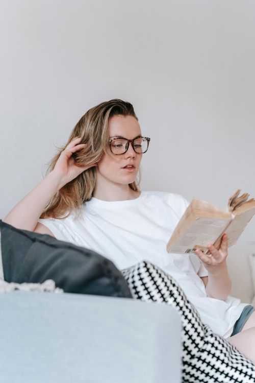 Free Low angle of focused female touching hair while reading book at spare time Stock Photo