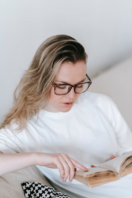 Free High angle of young female with long hair attentively reading book and sitting on sofa Stock Photo