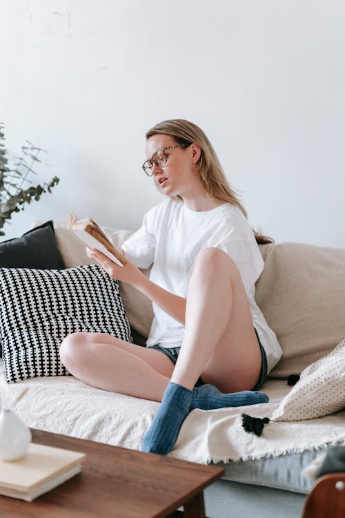 Free Blond with crossed legs reading book at home Stock Photo