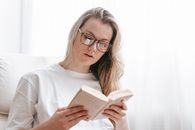 Young woman in eyeglasses reading book at spare time