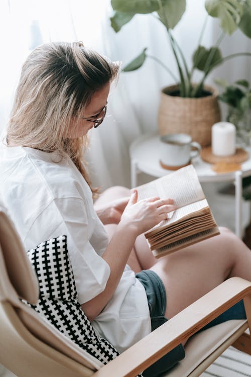 Free Focused woman reading book in armchair Stock Photo