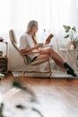 Young woman reading book in armchair near window
