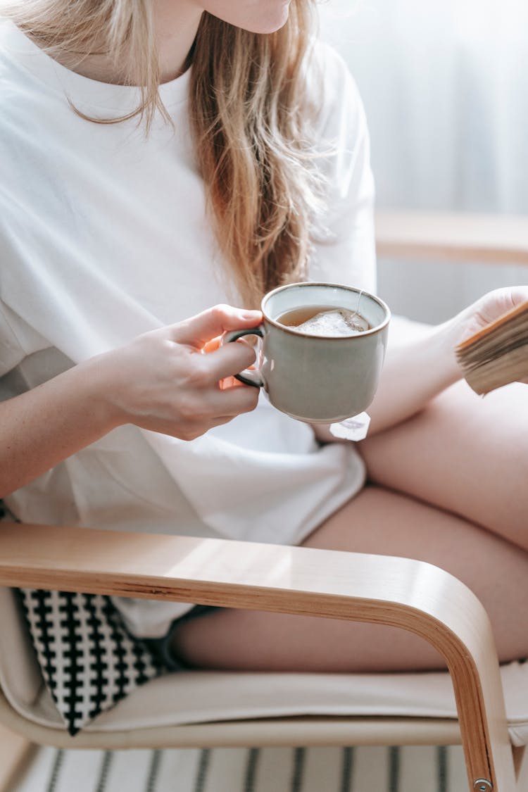 Crop Woman With Tea Reading Old Book In Armchair