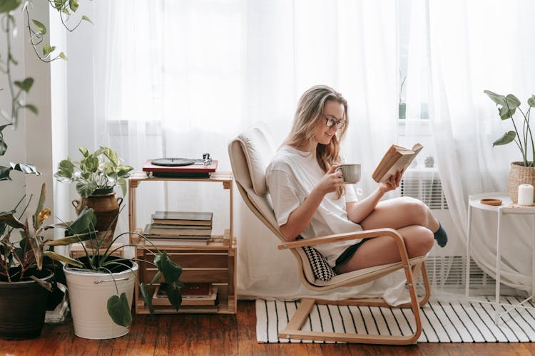 Smiling Woman With Hot Drink Reading Book At Home