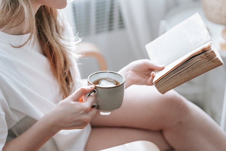 Crop Woman With Tea Reading Old Book In Room