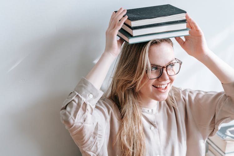 Cheerful Student In Eyewear With Books On Head