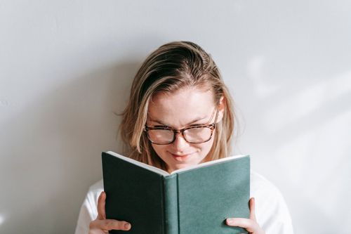 Free Interested young woman in glasses reading textbook while studying in sunshine on light background Stock Photo