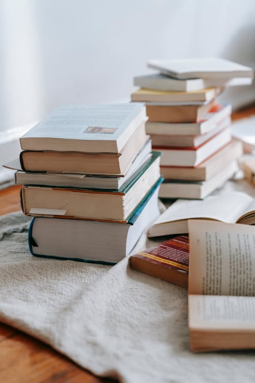 Free Stack of opened and closed books placed on white soft fabric on floor near wall in light room at home Stock Photo