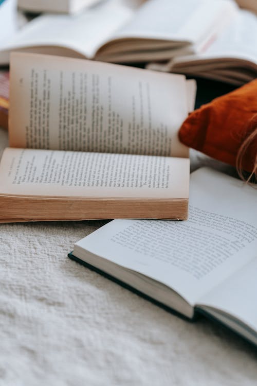 Heap of opened books with text placed on white fabric near colorful pillow in light room at home on blurred background