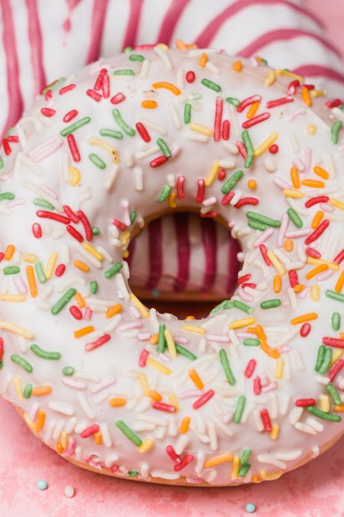 Free Close-up of a sprinkled donut with vibrant colors on a pink background. Stock Photo