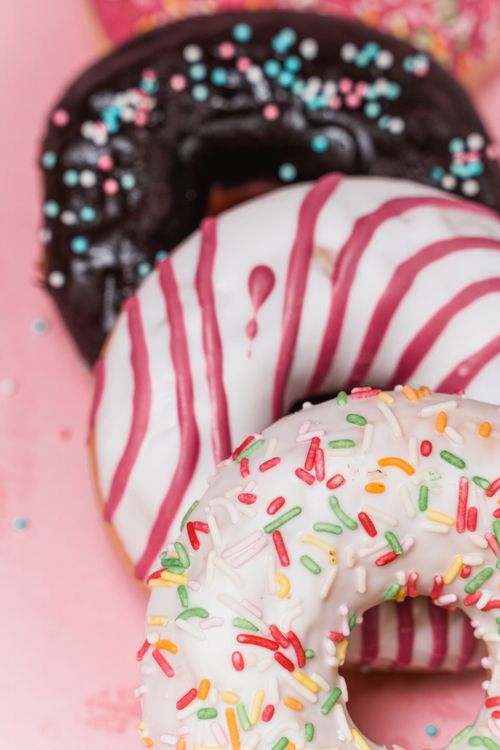 Free Close-up of delicious donuts with colorful sprinkles and striped icing on a pink background. Stock Photo