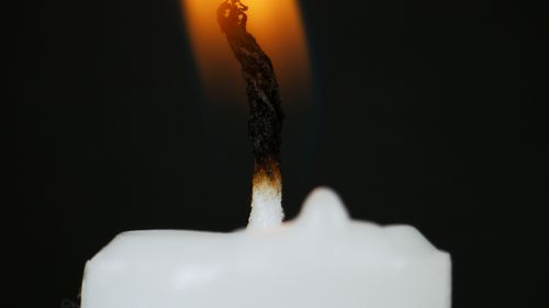 Free Close-up of a burning candle with a glowing flame and dark background. Stock Photo