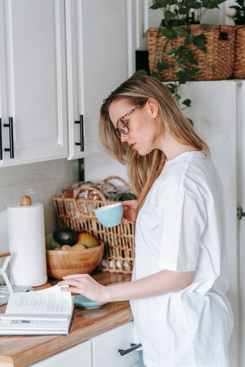 Free Side view of focused smart female in eyeglasses studying interesting book while having breakfast in modern kitchen Stock Photo