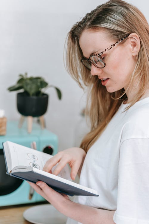 Intelligent woman in eyeglasses reading book at home