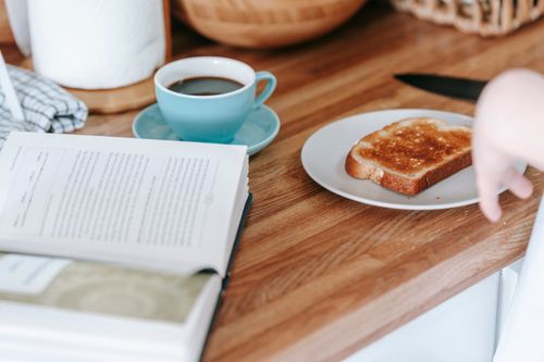 Free From above of crop anonymous female at table with tasty toast and cup of of fragrant strong coffee near book Stock Photo