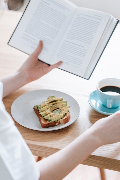 Free Crop woman with book and breakfast Stock Photo