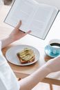 Crop woman with book and breakfast
