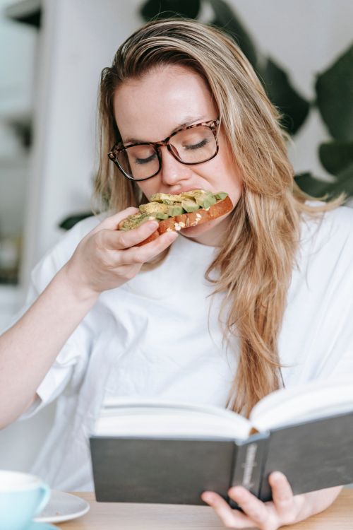 Reading Eating Young woman eating sandwich while reading book · Free Stock Photo