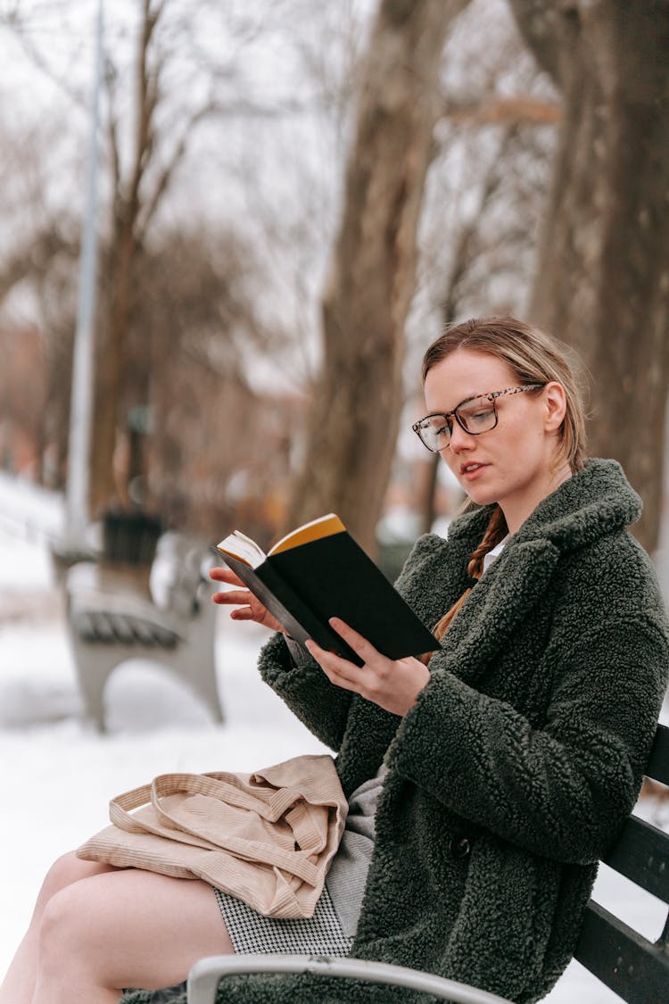 Young Woman Reading Book In Park In Winter