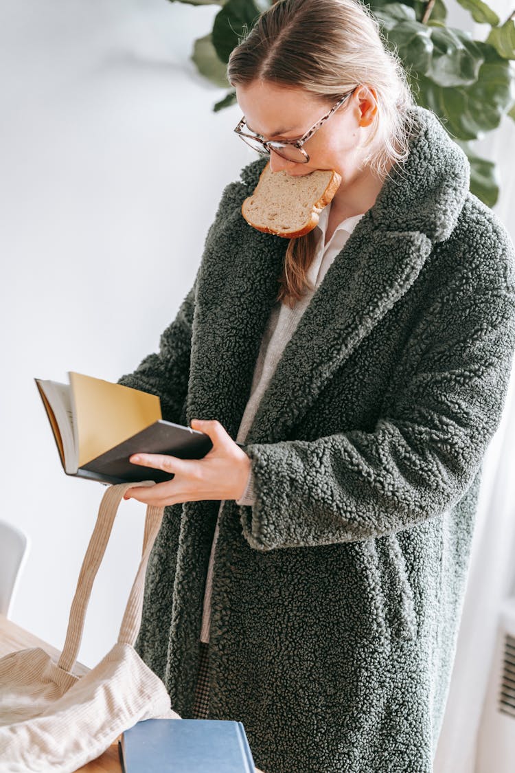 Woman Reading Book And Eating Bread In Light Room