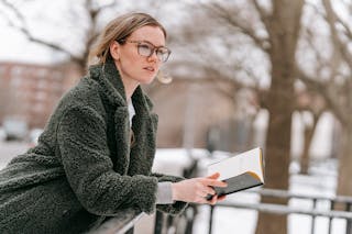 Young thoughtful woman with open book on street
