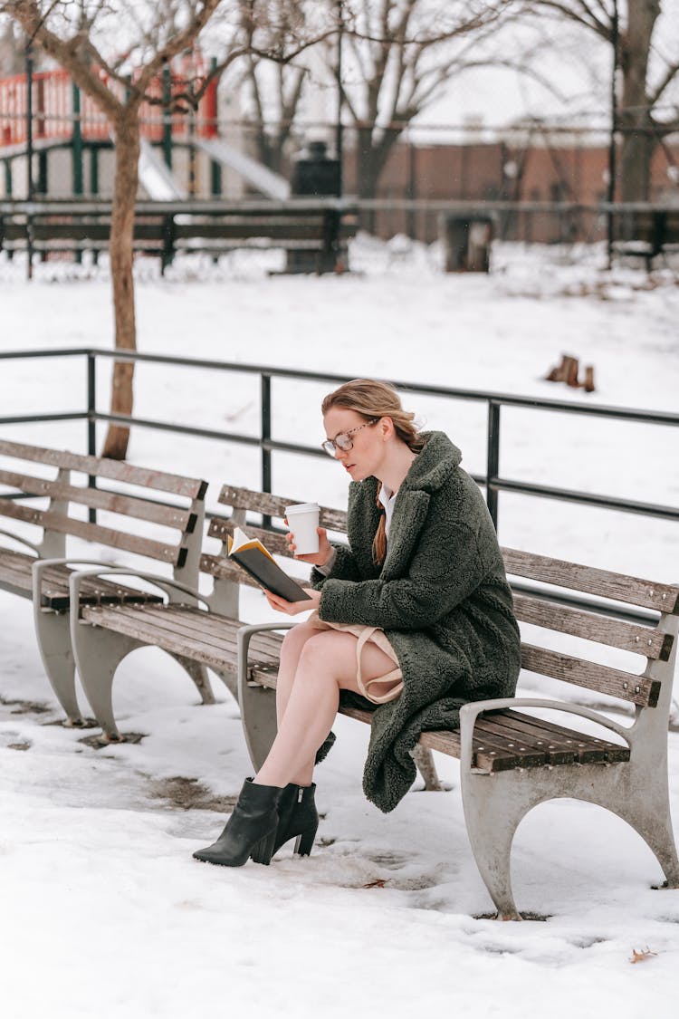 Attentive Student With Takeaway Coffee Reading Book In Winter Park