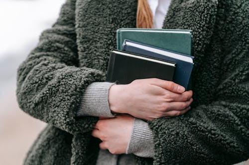 Free Faceless student in coat with assorted books Stock Photo