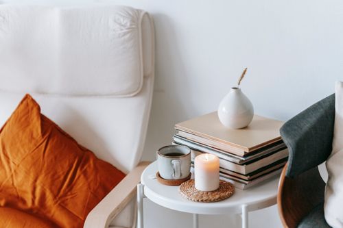Free Cup of tea and flaming candle against heap of books with dry spike in vase between armchairs at home on white background Stock Photo
