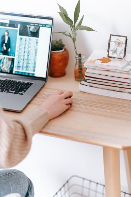 Free Crop anonymous remote employee working on netbook with photos on screen while sitting at table in house on white background Stock Photo