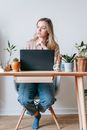 Contemplative young female distance worker looking away at table with netbook in house room on light background