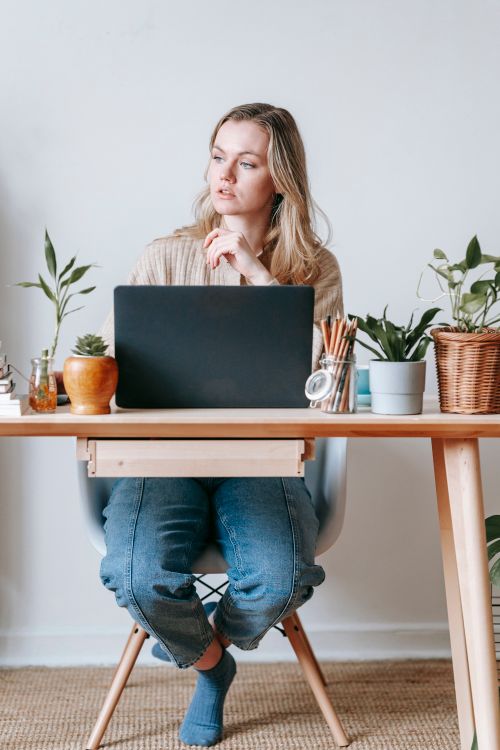 Free Contemplative young female distance worker looking away at table with netbook in house room on light background Stock Photo