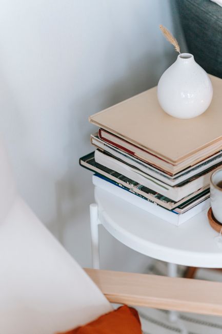 Ceramic vase with dried plant sprig on heap of textbooks on table in house on light background