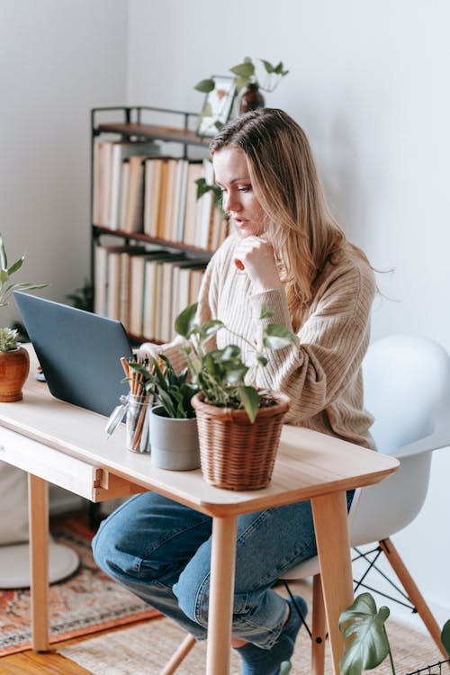 Free Thoughtful freelancer working on laptop at table in house Stock Photo