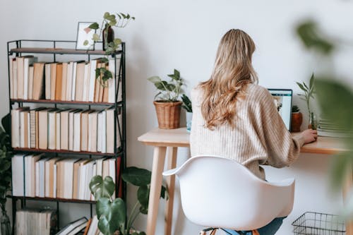 Unrecognizable freelancer working on laptop against bookcase at home