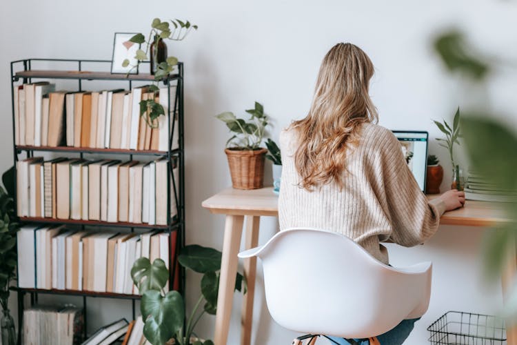 Unrecognizable Freelancer Working On Laptop Against Bookcase At Home