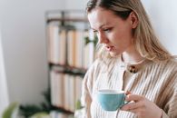 Crop focused young female with ceramic cup of hot beverage looking down in light house room