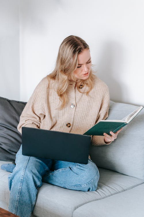 Focused woman reading notebook while loading laptop