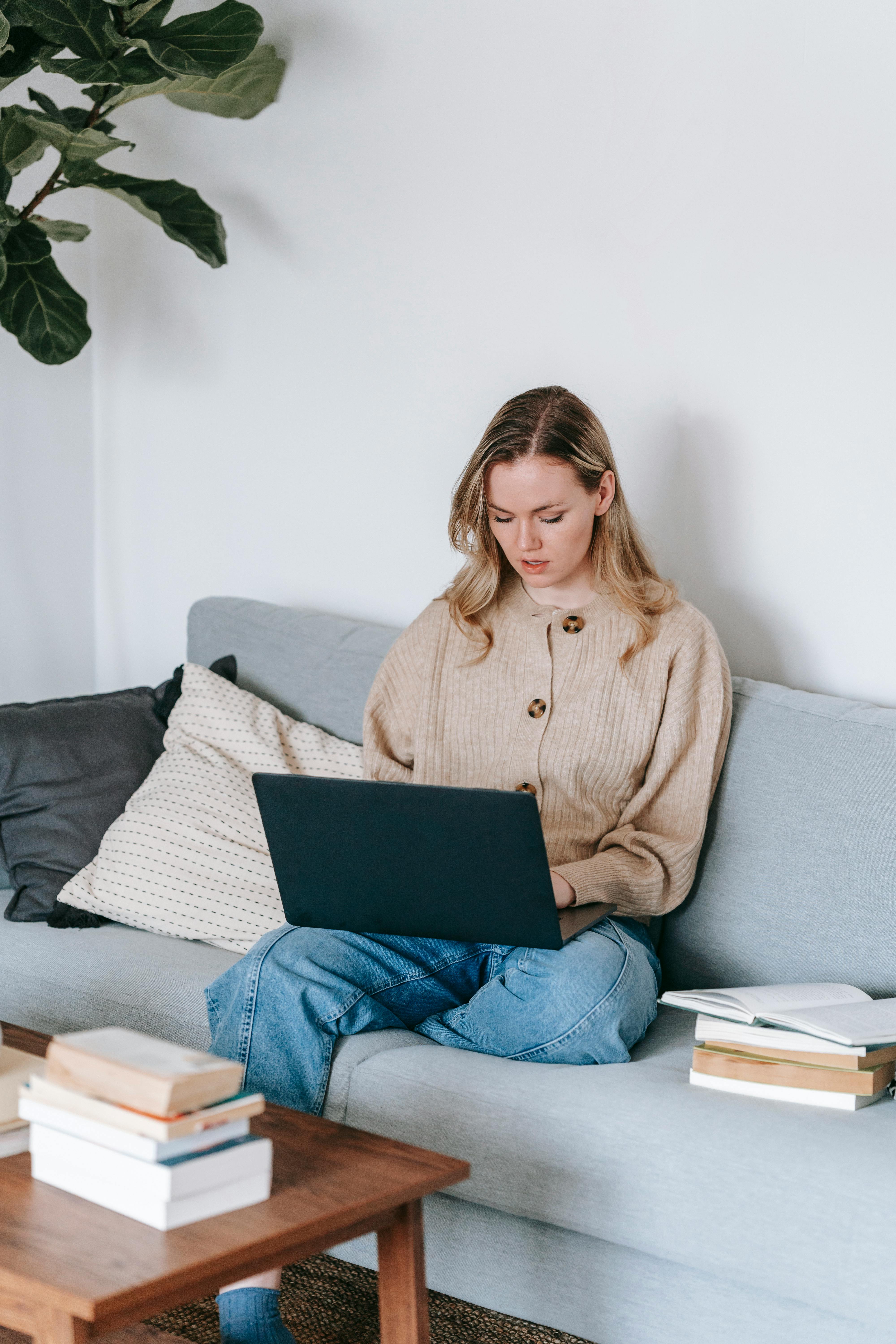 busy woman working with laptop on sofa with books