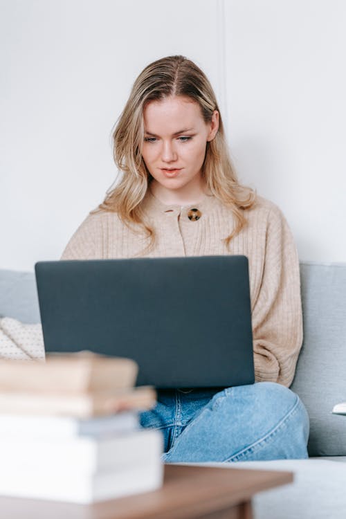 Free Young focused female using netbook while studying on sofa at table in apartment in daytime Stock Photo