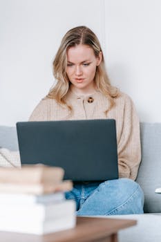 Young focused female using netbook while studying on sofa at table in apartment in daytime